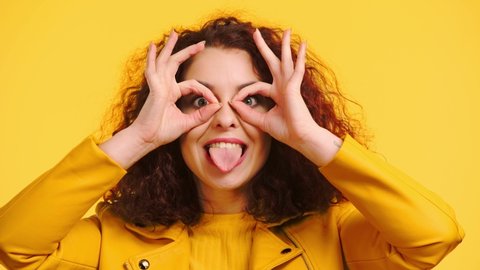 cheerful girl imitating eyeglasses with hands and grimacing isolated on yellow
