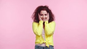 happy, flirty girl smiling while looking at camera isolated on pink