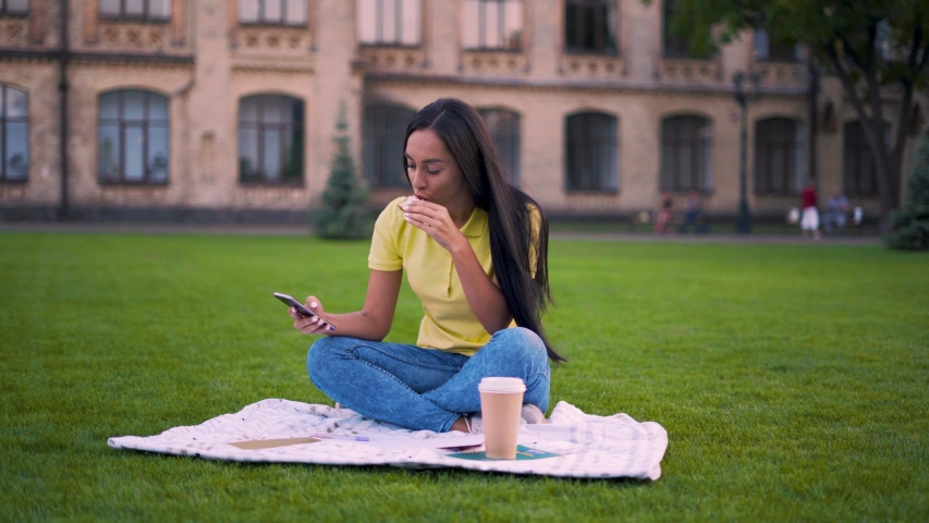 Young girl on a picnic. Girl scrolls the phone and eats a sandwich 4K