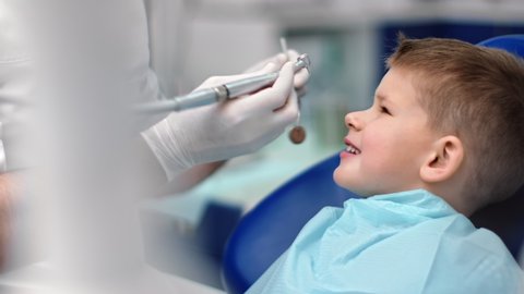 Hands in gloves of professional man dentist treating teeth to little boy. Child with toothache in stomatology armchair during cure close up. Shot on RED Raven 4k Cinema Camera