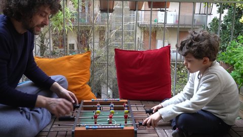 Europe, Italy , Milan - father and son five years at home during quarantine due n-cov19 Coronavirus outbreak - life stile in apartment - Playing soccer football table on the balcony