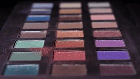 This closeup, macro video shows a makeup brush dipping into colorful eyeshadow powders on a makeup palette.