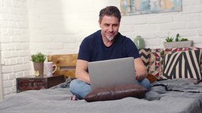 Stay at home and work in home office - Casual man sitting on bed working online from home with laptop computer.