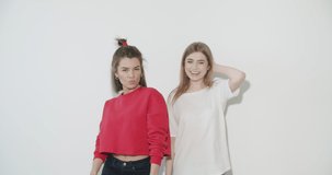 Two smiling crazy girl in summer clothes having fun. Young women dancing . Models posing on white wall background. Female showing positive face emotions. 4k video footage slow motion