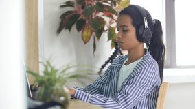 Young freelancer woman working at home, with a headphone typing on a laptop.