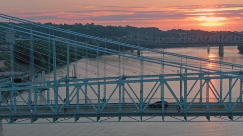 Aerial: Traffic crossing the John A. Roebling Suspension Bridge on the Ohio River at sunset. Cincinnati, Ohio, USA. 21 September 2019 