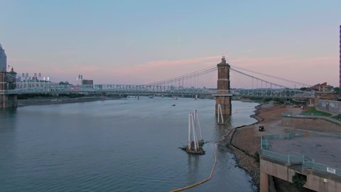 Aerial: Downtown Cincinnati and the John A. Roebling Suspension Bridge on the Ohio River at sunset. Cincinnati, Ohio, USA. 21 September 2019 