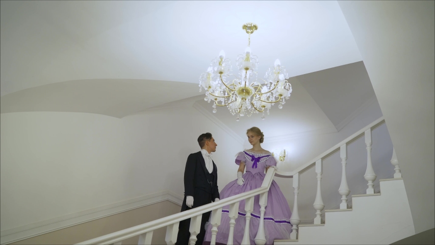 A young couple in dresses goes down the stairs. A young couple in the images of the times of the XIX century.
