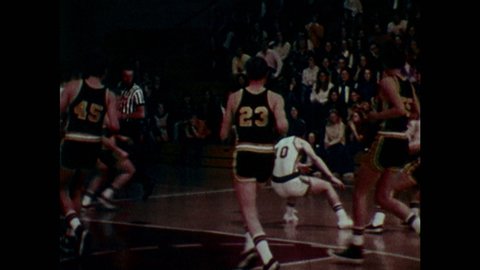1970s: Basketball players' feet move about the court during a game. Man greets player on sidelines. Man sits and begins talking. Man holds up socks while talking.
