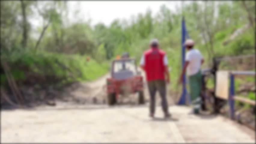 Ferry boat for transport agricultural machinery across the river. Tractor with attached agricultural sprayer is leaving from ferry boat on shore.
