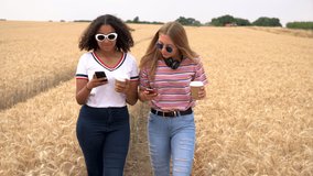 Slow motion video clip of pretty blonde girl and mixed race teenager young women wearing sunglasses drinking coffee and taking selfies on their smart phones for social media