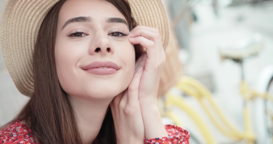 Graceful young woman with long shiny hair gladly posing while walk outside in good mood. Outdoor close-up photo of pleased girl in trendy summer hat enjoying sunshine.
