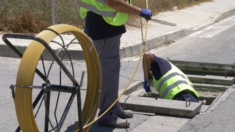Operators in reflective yellow vests pick up fiber optic cable from a manhole on the street.