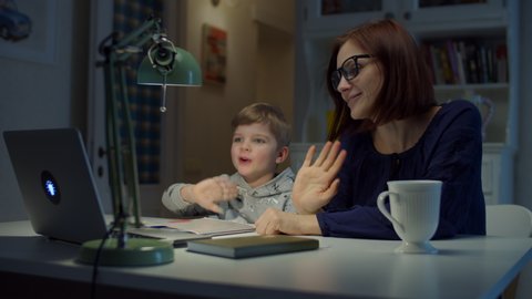 Young 30s mother making online homework with preschooler son at home. Woman in glasses and young boy studying online with laptop and notebook. Online education process. 