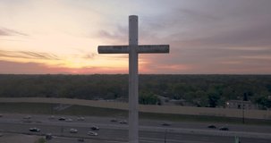 Aerial drone view 4K video with pull back or fade away shot of a giant cross next to a busy highway with cars and trucks going by at sunrise in central Florida