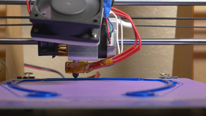3d printer being used to print PPE face shields for health care workers during the COVID-19 pandemic.  Extruder can be seen moving side to side while the heated print bed moves towards camera.  | Shutterstock HD Video #1049786869