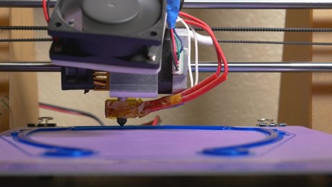 3d printer being used to print PPE face shields for health care workers during the COVID-19 pandemic.  Extruder can be seen moving side to side while the heated print bed moves towards camera. 