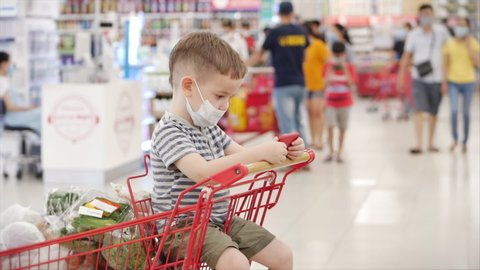 Mom with children makes purchases in the hypermarket,child sits in a protective mask against viruses,child sits in a grocery cart,watches videos,cartoons on phone. Concept People,Coronavirus,Epidemic.