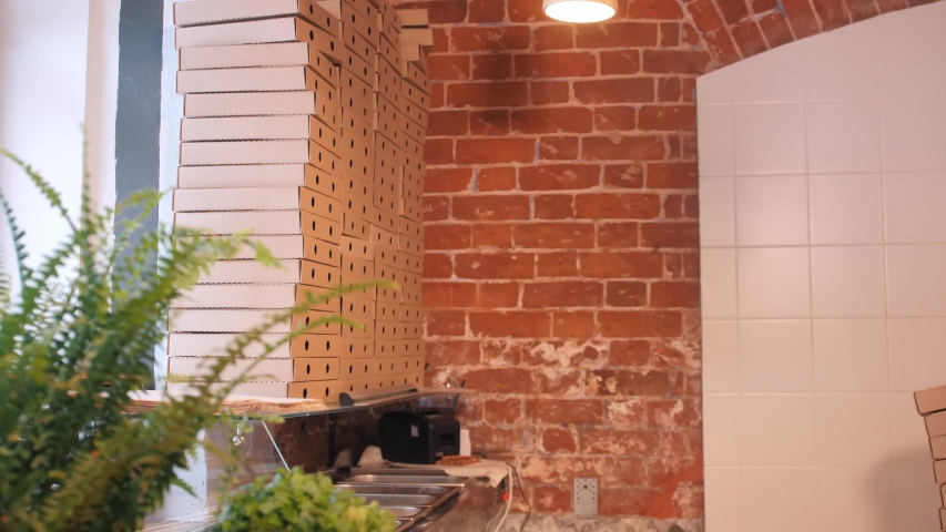 tall pizzeria worker carries empty pizza cardboard boxes and puts on stack located near cafe high window close view
