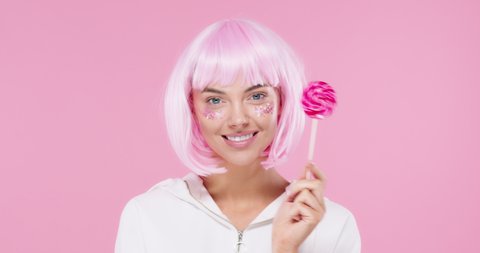 Beautiful female model with trendy pink hair style and beautiful glitter makeup holding sweet lollipop