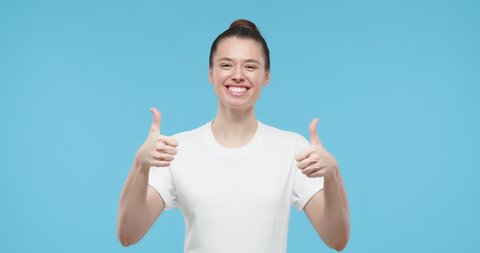 Young woman pointing to her white t-shirt with thumbs up gesture, showing empty space for your text or logo, isolated on blue background