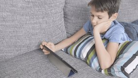 Boy lying on sofa with digital tablet computer at home. Technology, ditance education, online learning, playing games concept