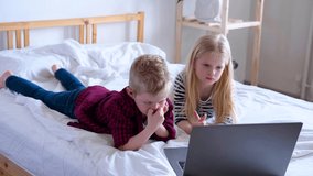 Distance learning online education. Schoolboy and girl studying at home with digital tablet laptop notebook and doing school homework. Sitting on bed with training books