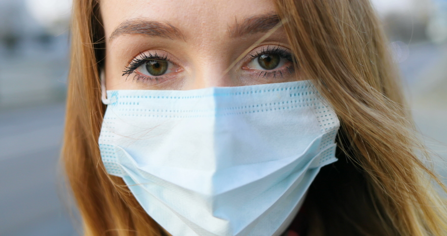 Close up of face of Caucasian young beautiful woman with respiratory virus wearing mask at street outdoor in city. Portrait of protected sad girl looking at camera. Healthcare and safety concept. Royalty-Free Stock Footage #1049800411