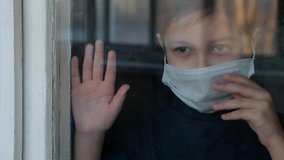 Young boy in a medical mask looks out the window. Self-isolation in quarantine, coronavirus, covid 19. - Powered by Shutterstock - Get 15% off with code: PIKWIZARD15