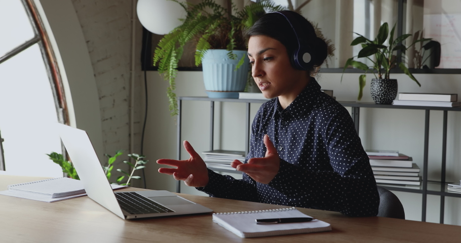 Young indian business woman wearing headphones communicating by video call. Ethnic businesswoman speaking looking at laptop computer, online conference distance office chat, virtual training concept.