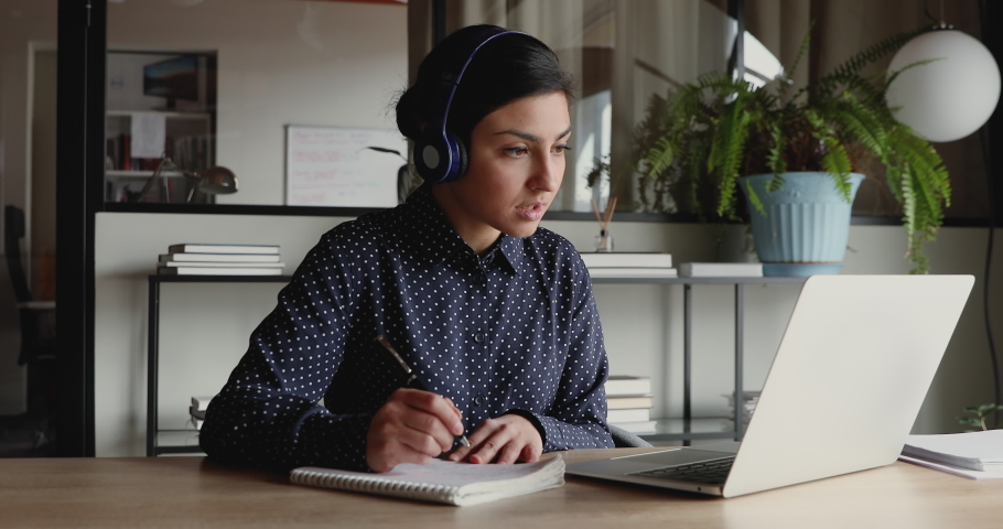 Female indian distant worker wears headphones video calling makes notes, elearning with online teacher, working from home office attending remote conference meeting. Videoconference training concept. | Shutterstock HD Video #1049816992