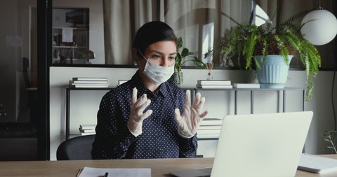 Young indian business woman wearing medical gloves and face mask communicating by video call on laptop computer. Online conference distance remote home office during coronavirus covid 19 quarantine.