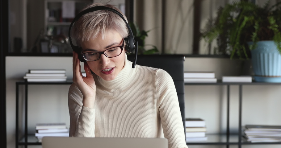 Confident female office worker wears headset conference video calling looking at laptop computer. Young businesswoman customer service manager speaking to webcam communicating in distance remote chat. | Shutterstock HD Video #1049817007