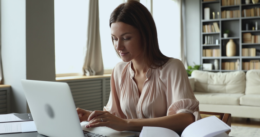 Focused young woman sitting at table, typing message on computer, studying on online courses. Concentrated businesswoman communicating with client or working remotely on laptop from home alone. Royalty-Free Stock Footage #1049817073