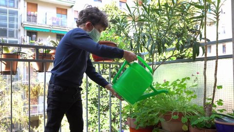Europe, Italy , Milan - children boy  five yewith mask ars at home during quarantine due n-cov19 Coronavirus outbreak - life stile in apartment - water the plant and flowers on the balcony