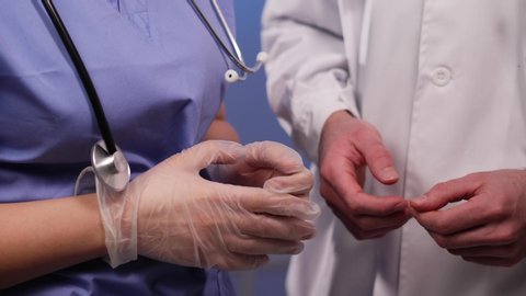 Male medical professional doctor in a lab coat being a pervert, trying to hit on a nurse in scrubs , and a stethoscope at work, by touching her gloved hands, and she is rejecting him multiple times.
