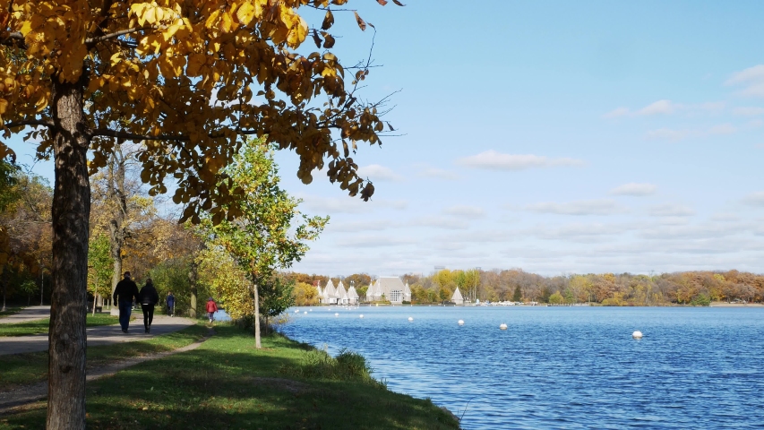 Walking and bike path along the beautiful Lake Harriet in Minneapolis on a sunny afternoon with colorful autumn leaf foliage, blue sky and fluffy white clouds.
