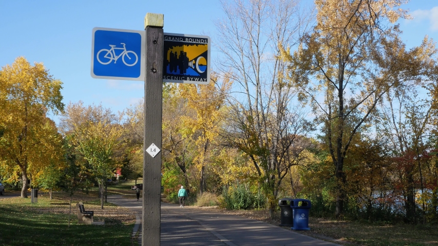 Bike path along Lake Harriet in Minneapolis, Minnesota on an autumn afternoon with people out for exercise and relaxiation with zoom in on blue sign.