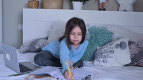 Distance learning online education. Schoolgirl  with digital tablet laptop notebook and doing school homework. Sitting on bed with training books. Home school. 4k video . copy space