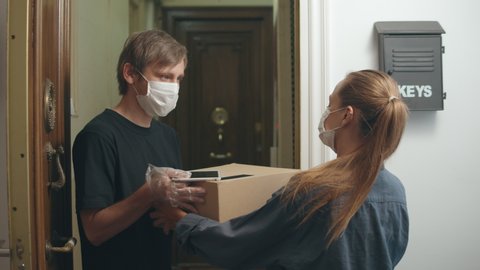 postman or delivery man carry small box deliver to young woman customer at home. Man wearing mask prevent covid or coranavirus quarantine pandemic. Social distancing home isolation work concept.