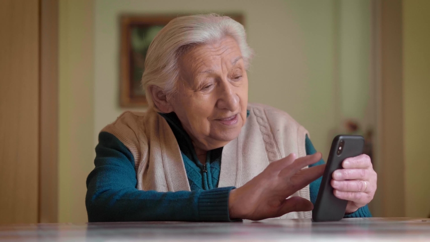 An authentic shot of a happy grandmother making a video call to relatives with a smartphone at home. Concept of technology, modern generation, family, connection, authenticity. Royalty-Free Stock Footage #1049838430