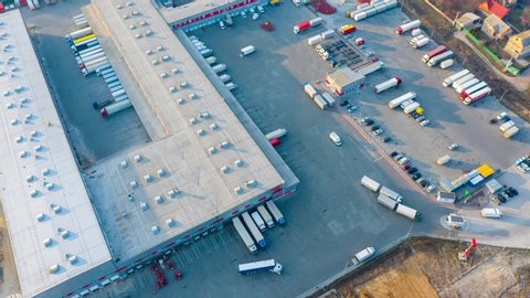 Aerial hyper lapse (hyperlapse - time lapse) of the large logistics park with warehouse, loading hub and semi trucks with cargo trailers standing at the ramps for load/unload goods