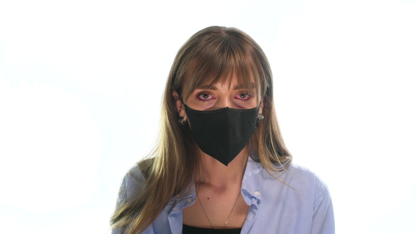 on a white background, a girl with red sore eyes pulls off a black mask from her face to ease her breathing, and red inflammatory processes are visible around her mouth Royalty-Free Stock Footage #1049844823