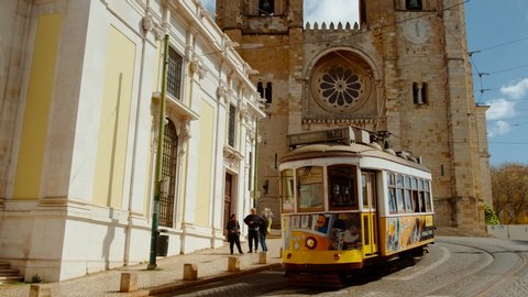 LISBON, circa 2019 - Tilting shot of Alfama district in Lisbon, Portugal featuring a picturesque tram and the imposing Lisbon cathedral dating to 1147