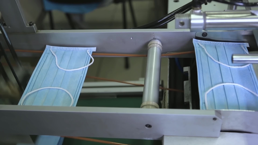 Production of disposable medical clothing for protection against the virus. Medical mask on conveyor belt in the workshop of factory for production of medical clothing. Manufacture of medical masks. Royalty-Free Stock Footage #1049845741