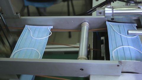 Production of disposable medical clothing for protection against the virus. Medical mask on conveyor belt in the workshop of factory for production of medical clothing. Manufacture of medical masks.