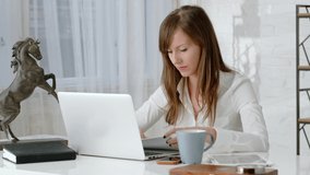 Young business woman working at desk with laptop computer in home office. Slow pan to right.