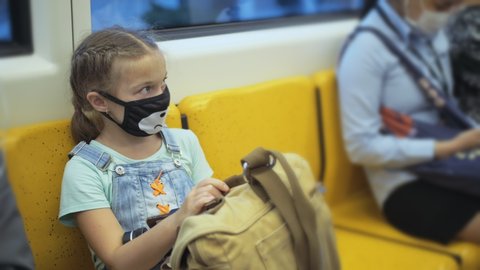 Little girl travel caucasian ride at overground train airtrain with wearing protective medical red mask. Child baby tourist at airtrain with respirator. Pandemic Coronavirus covid-19. People in mask.