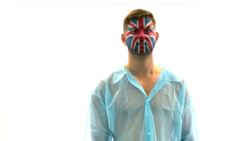 Corona Virus Lockdown. Sad male medical patient with a painted UK flag on his face. Pandemic, epidemic, coronavirus. The man on a white background. Sad, sick football fan on quarantine. Union Flag.