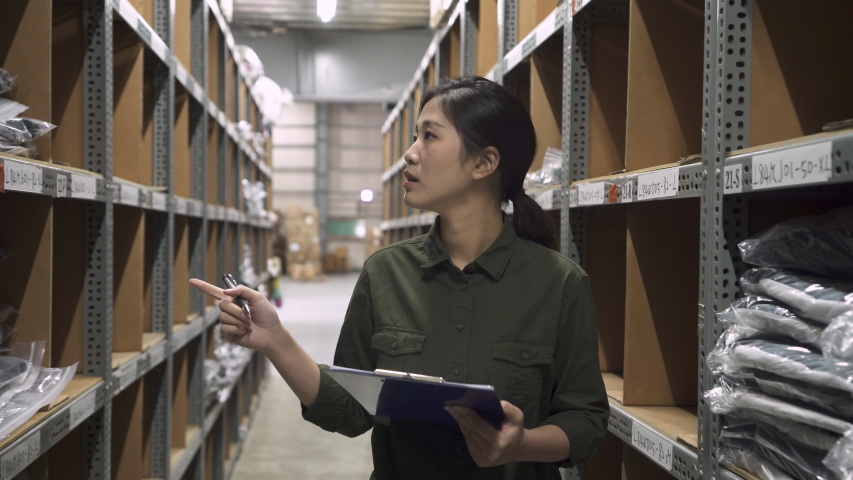 elegant asian female warehouse worker with clipboard doing stock taking job and writing report. young woman employee holding touch pad walking out and meet colleague asking problem in stockroom. Royalty-Free Stock Footage #1049849590